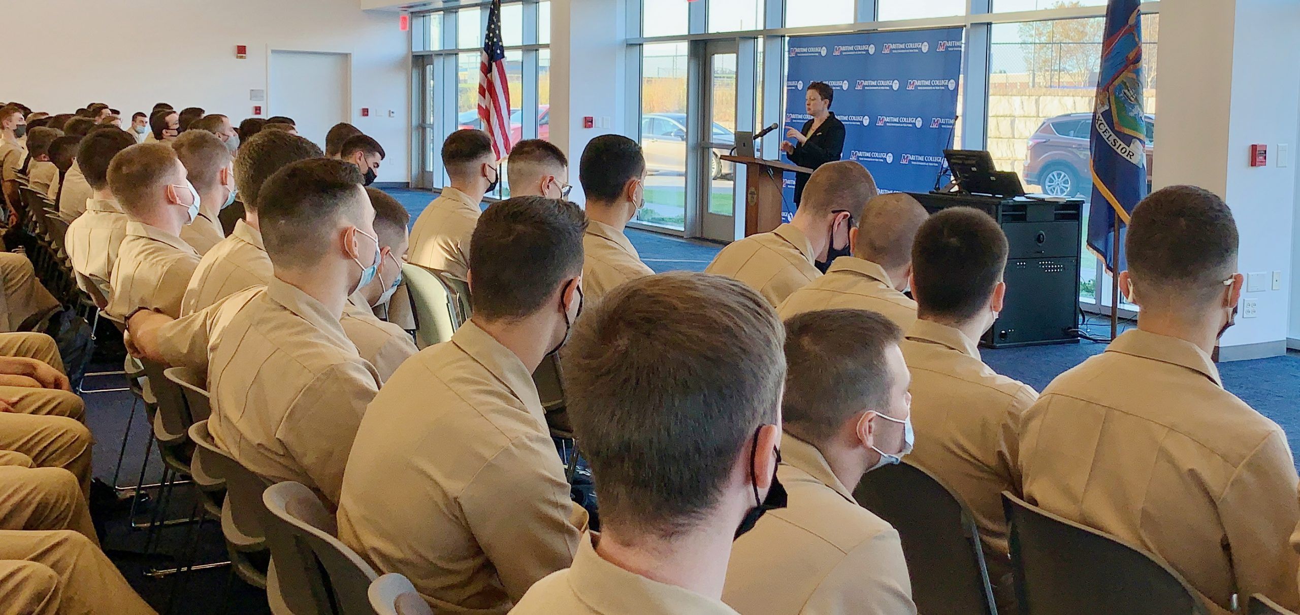 DuLong behind a podium speaking before an audience of young men in beige uniforms